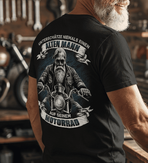 Ein älterer Mann mit schwarzem T-Shirt und weißem Bart steht in einer Motorrad Garage