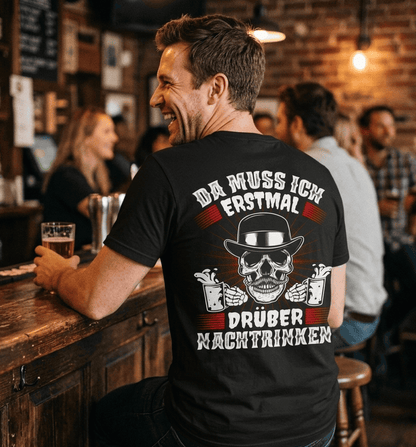 Mann in schwarzem T-Shirt mit Spruch Da muss ich erstmal drüber nachtrinken sitzt an der Bar
